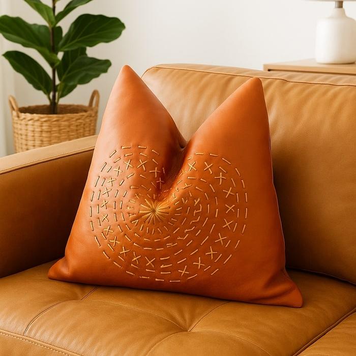 Tan leather cushion cover with gold mandala embroidery on a brown leather sofa.