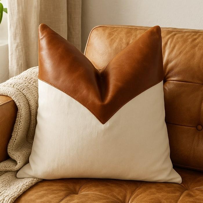 Tan leather and cream canvas cushion cover with a V-shaped design on a brown leather sofa.