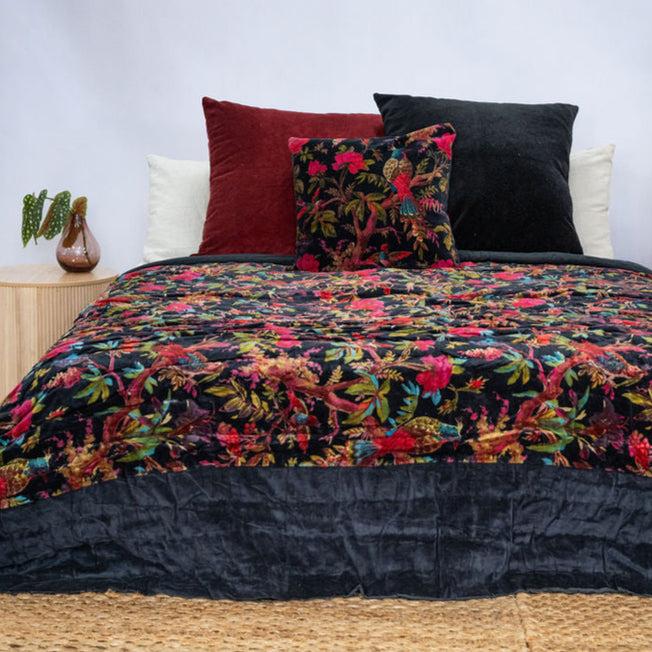 Black cotton velvet quilt with vibrant fuchsia, teal, and gold botanical bird print, styled with matching cushions.