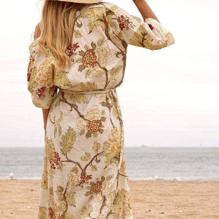 Woman in a beige cotton kimono with earthy floral print, tied at the waist, on a beach.