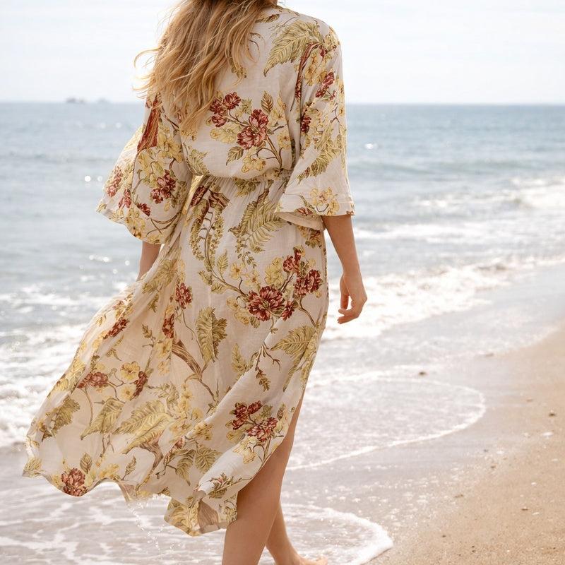 Woman in a flowing, cream cotton kimono with red and yellow floral print, walking on a beach.