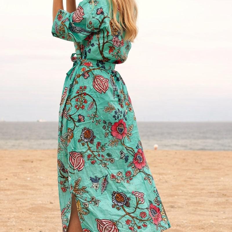 Turquoise cotton kimono with colorful floral and bird of paradise print, tied at the waist, worn on a beach.