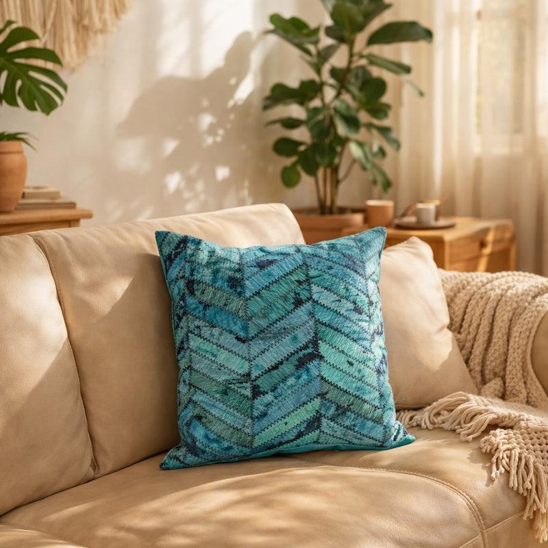 Teal cowhide patchwork cushion cover with chevron pattern on a beige leather sofa.