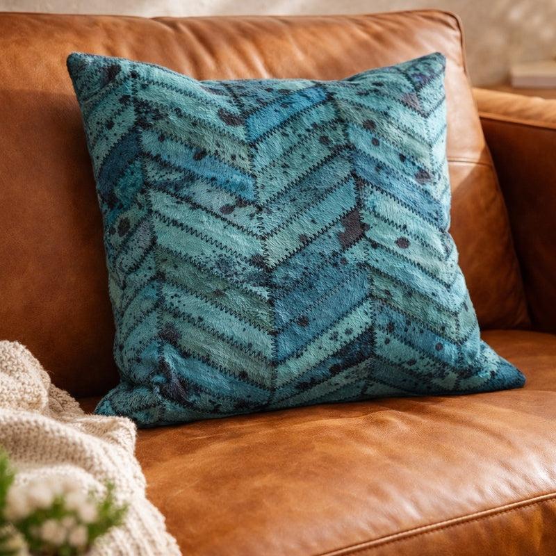 Teal blue patchwork cowhide cushion cover with chevron pattern on a brown leather sofa.