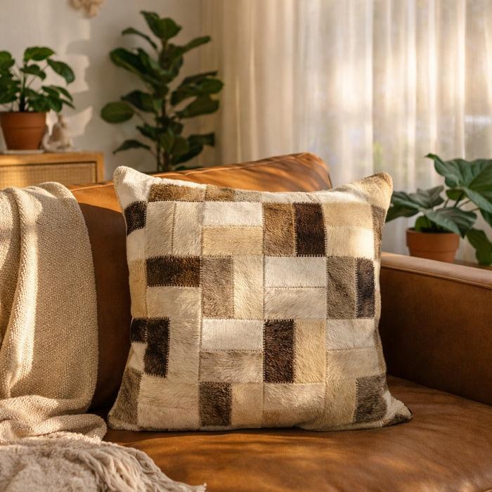 Neutral cowhide leather checkerboard cushion cover on a brown sofa, featuring cream, beige, and brown patches.