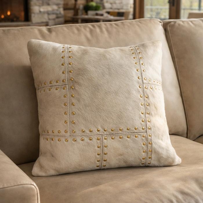 Ivory cowhide leather cushion cover with brass stud detailing, 40x40cm, on a beige sofa.
