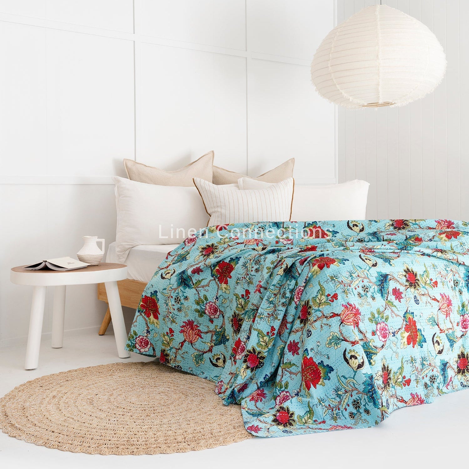 Tropical blue Kantha quilt with red floral and bird patterns on a bed in a bright room.