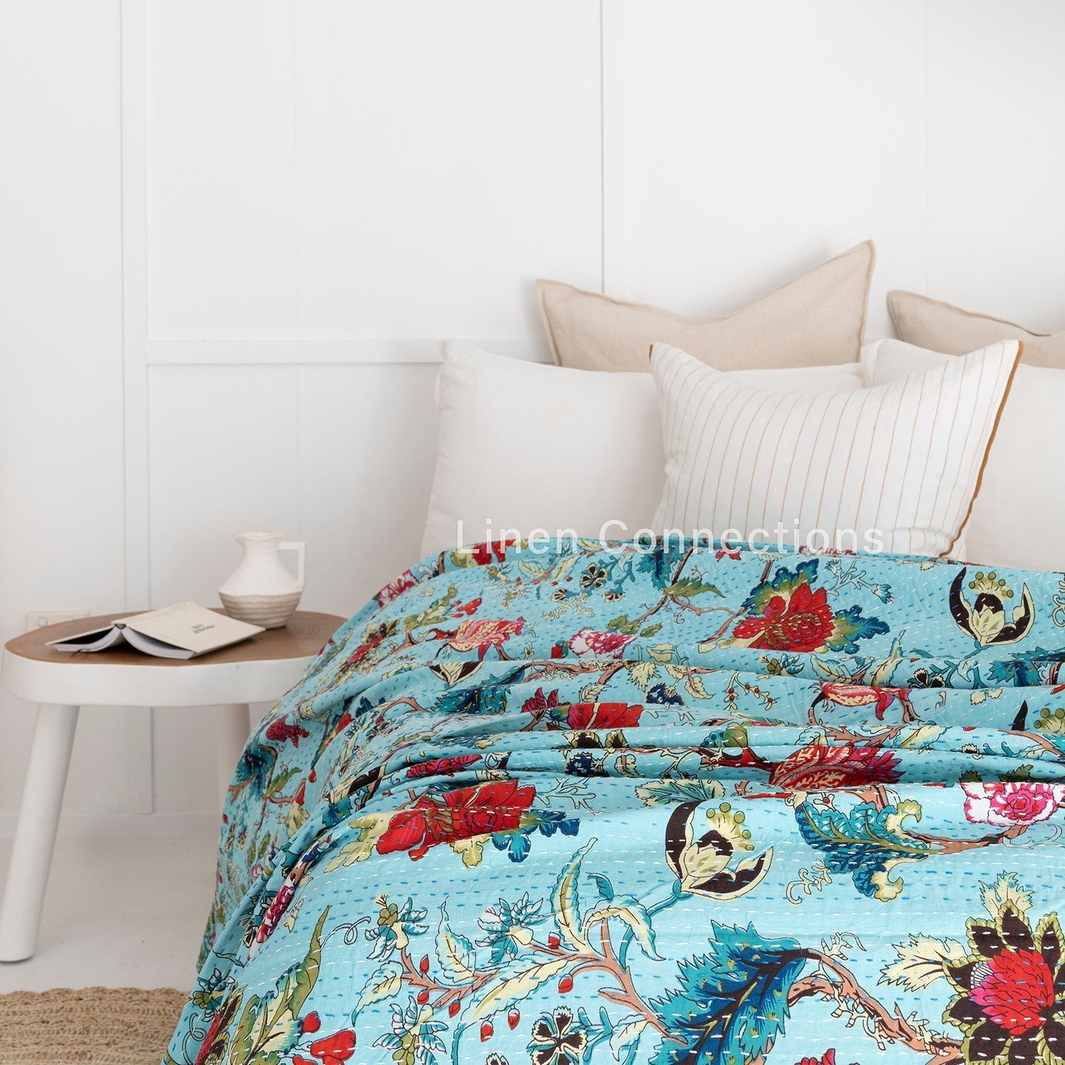 Tropical blue Indian Kantha quilt with vibrant red, green, and yellow floral patterns on a bed.