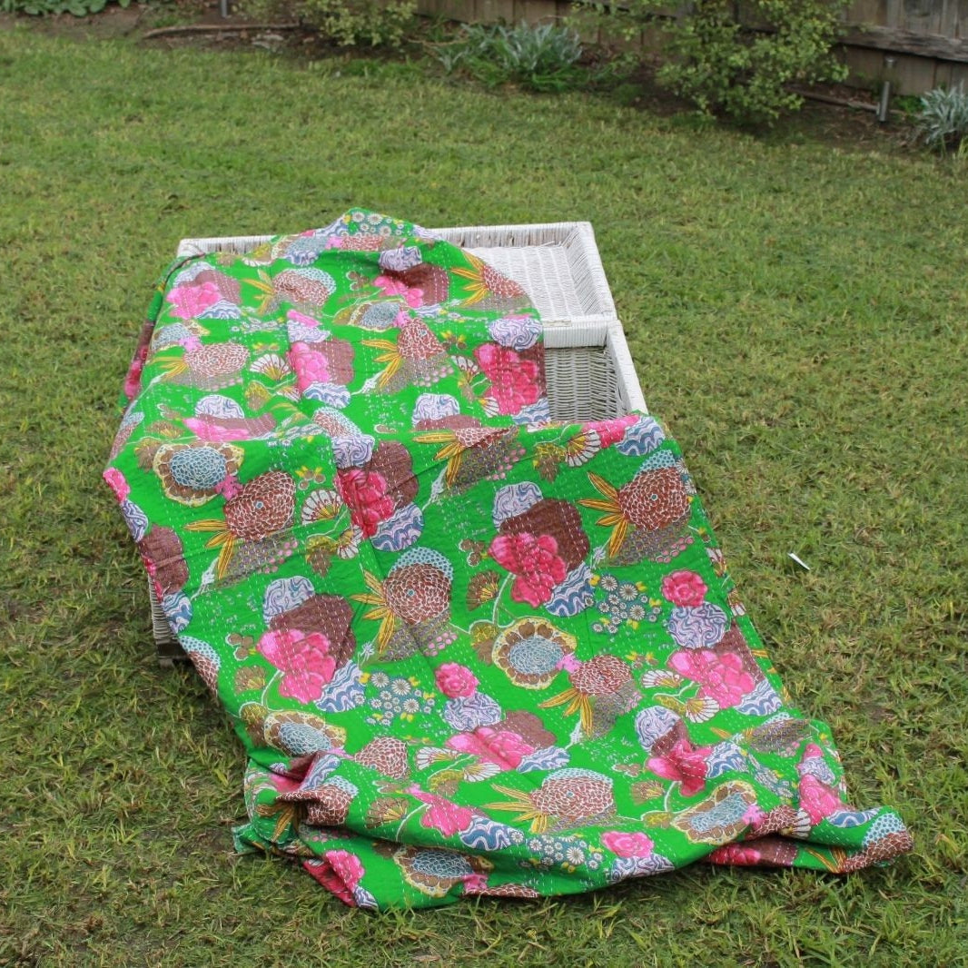 Vibrant green Boho Kantha quilt with pink, blue, and brown floral patterns draped over a white basket on grass.