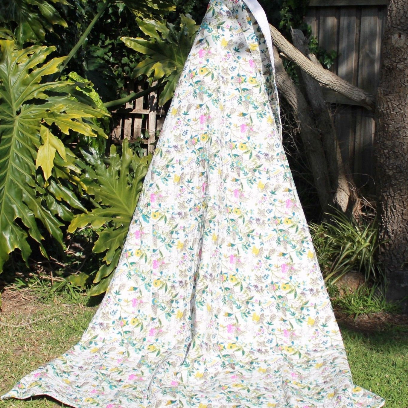 White cotton Kantha blanket with colorful floral and bird patterns, draped outdoors.