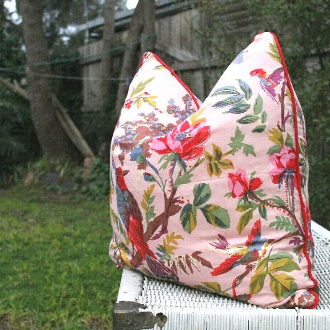 Pink cotton cushion cover with colorful floral and bird pattern, red piping, and zipper closure.