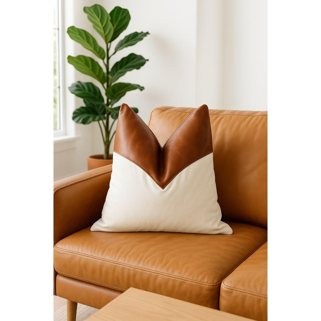 Tan leather and cream canvas cushion cover with a V-shaped design on a brown leather sofa.