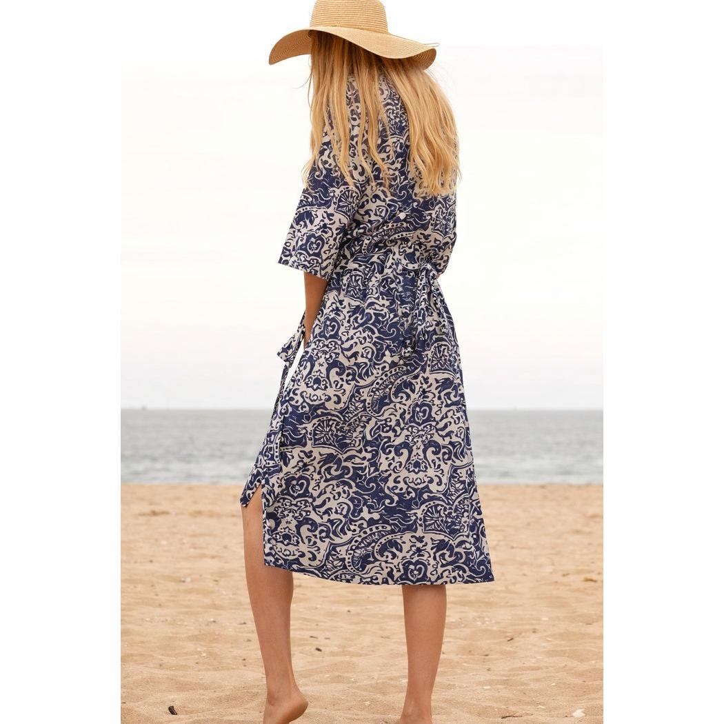Woman in indigo blue and white cotton kimono robe with bird of paradise print, tied at waist, on a sandy beach.