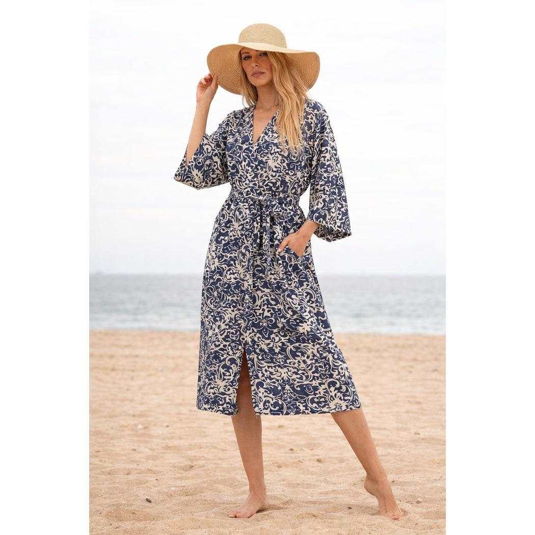 Woman in indigo blue and cream cotton kimono with bird of paradise print, tie waist, and pockets, on a beach.
