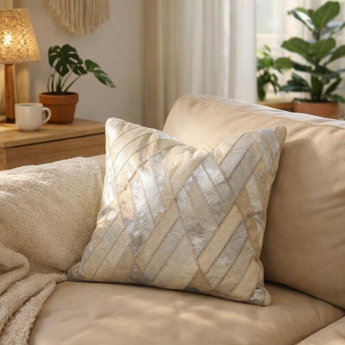 Ivory and silver cowhide leather cushion cover with a diagonal patchwork design on a beige sofa.