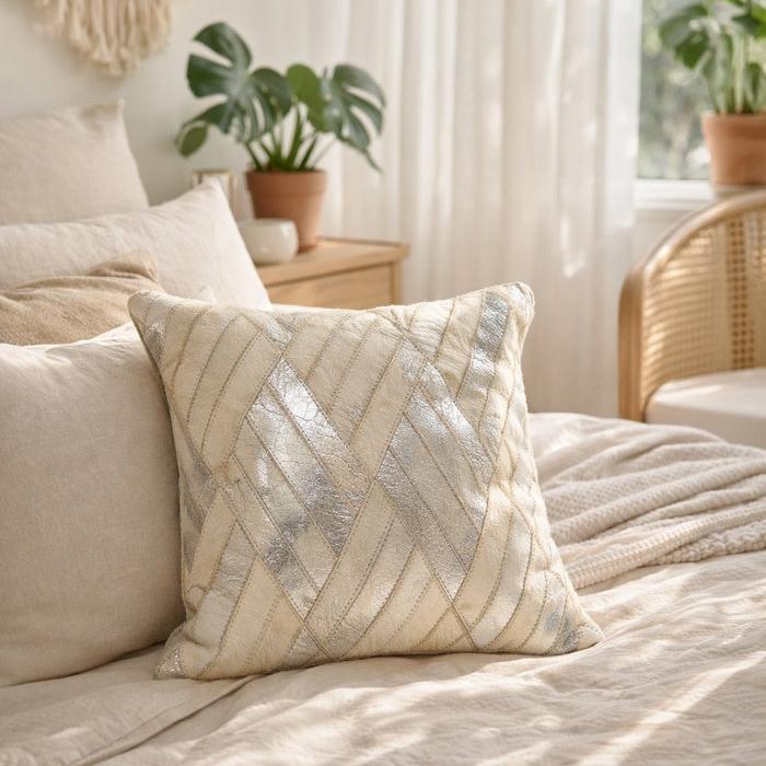 Ivory and silver cowhide leather cushion cover with a diagonal patchwork design on a bed.