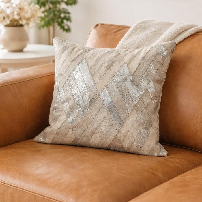 Ivory & silver cowhide leather cushion cover with diagonal patchwork design on a brown leather sofa.