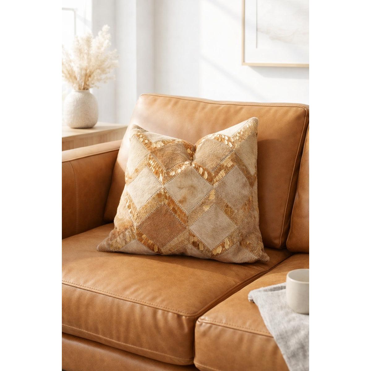 Boho gold check cowhide leather cushion cover with tan and neutral patchwork, displayed on a brown leather sofa.