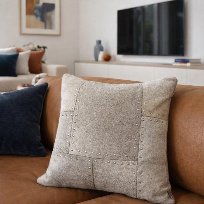 Grey studded patchwork cowhide leather cushion cover on a brown sofa.