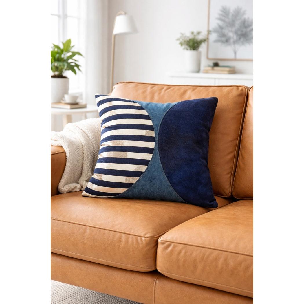 Handmade navy and silver striped cowhide cushion cover with curved panels on a tan leather sofa.