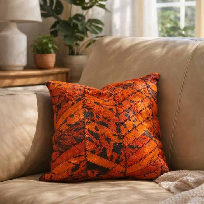 Orange and black patchwork cowhide cushion cover on a beige leather sofa.