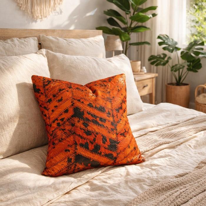 Orange & black patchwork cowhide cushion cover on a neutral bed in a bedroom.