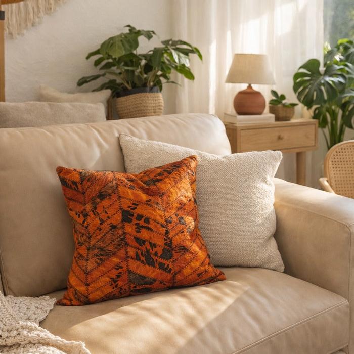 Luxury orange and black patchwork cowhide cushion cover on a beige sofa, adding warmth and texture.