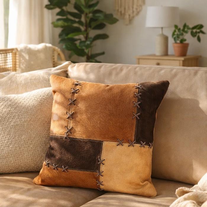 Tan & chocolate cowhide patchwork cushion cover with rustic cross-stitch lacing on a sofa.