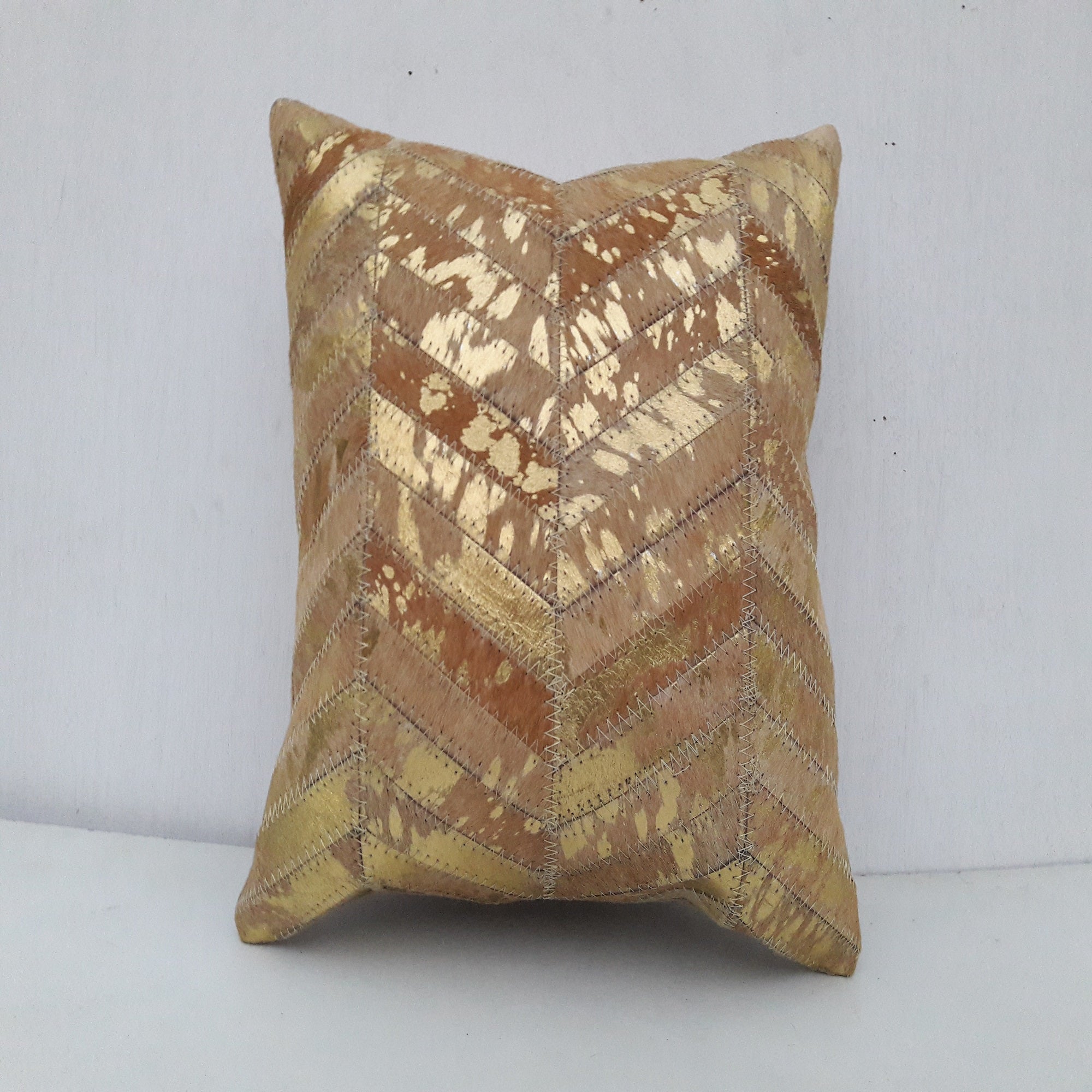 Golden exotic cowhide cushion cover with a chevron patchwork design, featuring natural brown and metallic gold tones.