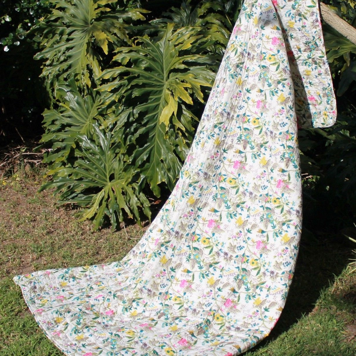 White Grey Goose Kantha blanket with colorful vintage floral print, draped outdoors.