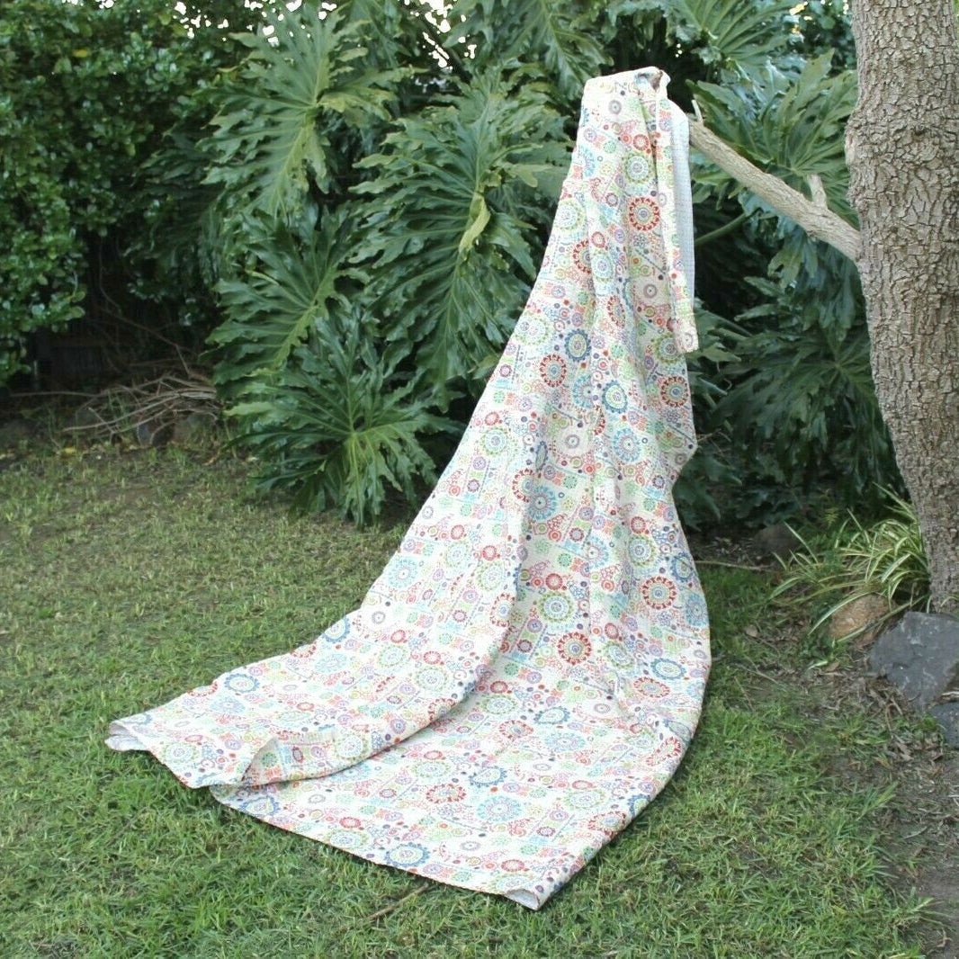 Colourful Circles Kantha Quilt, a handcrafted reversible cotton throw with vibrant circular patterns, draped outdoors.